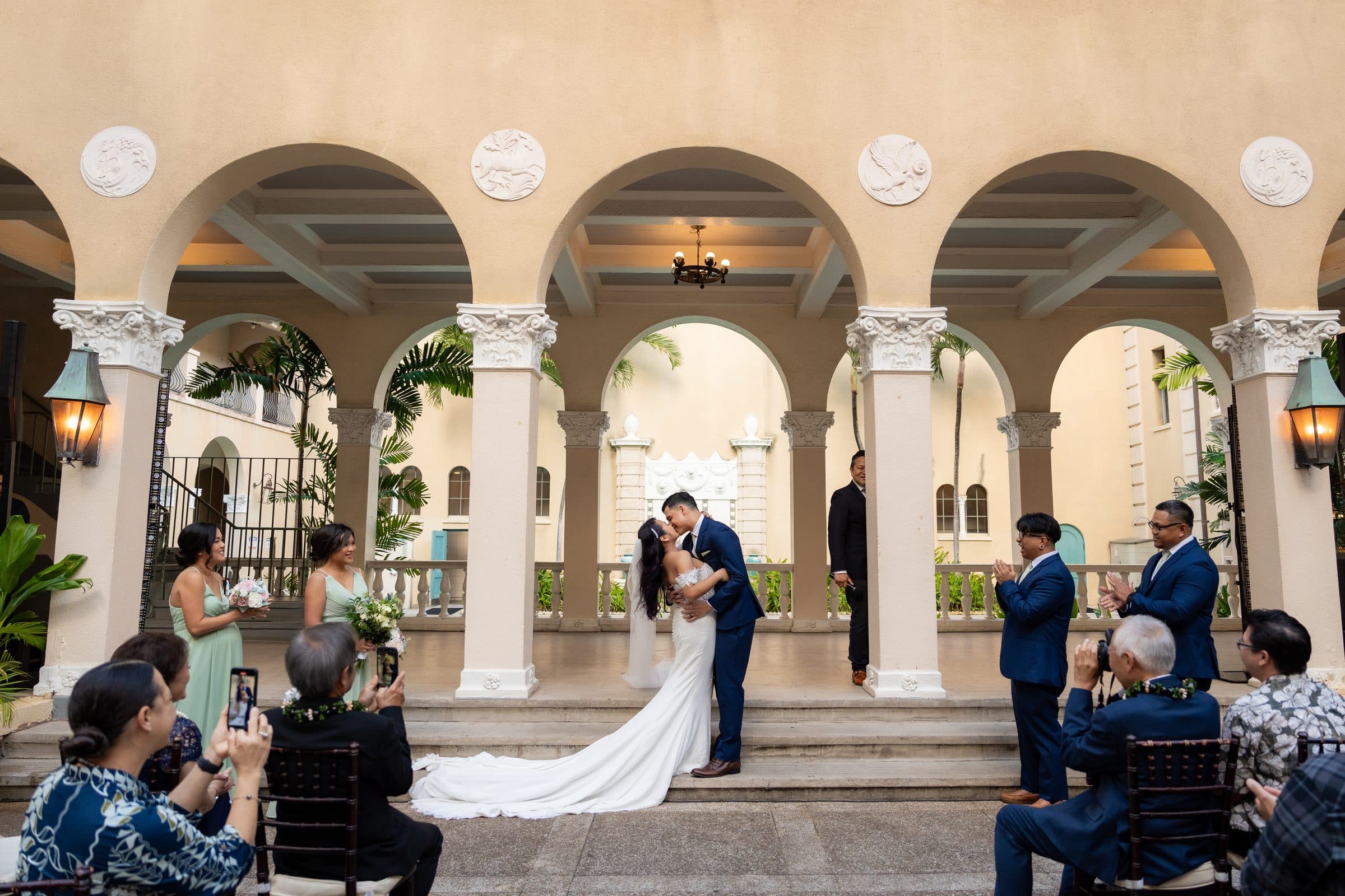 Adrianne and Ross kiss under the courtyard arches as their guests watch.