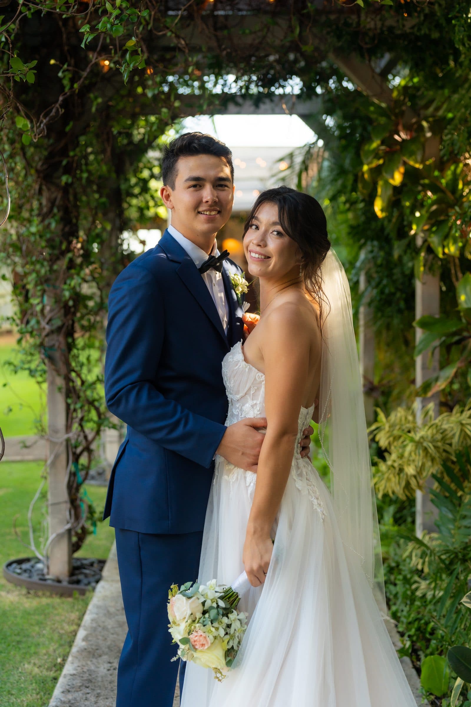 Nova and Cole stand together under a vine-covered pergola.