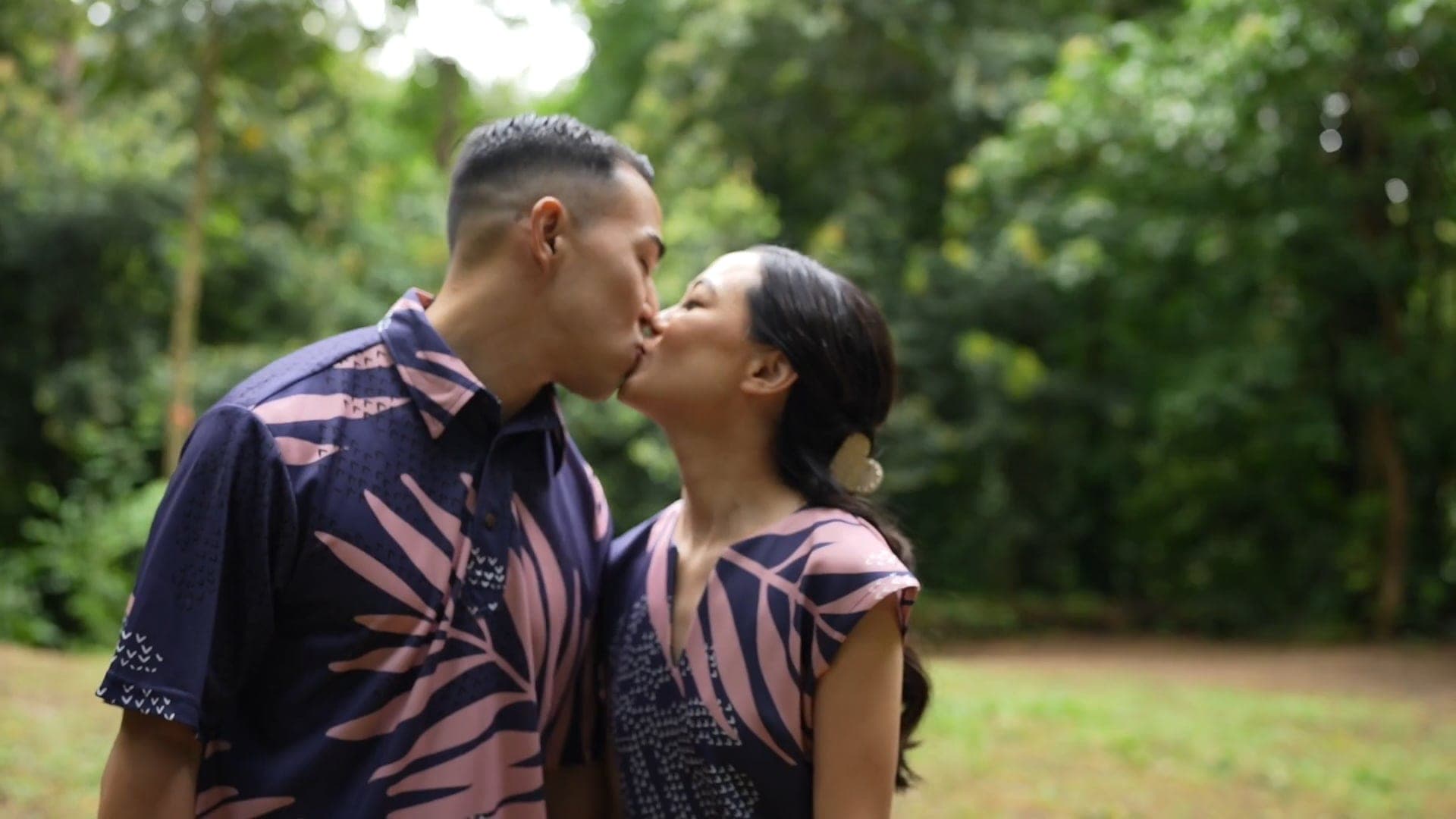 Amber and Darren, in matching floral prints, kiss in a green park.