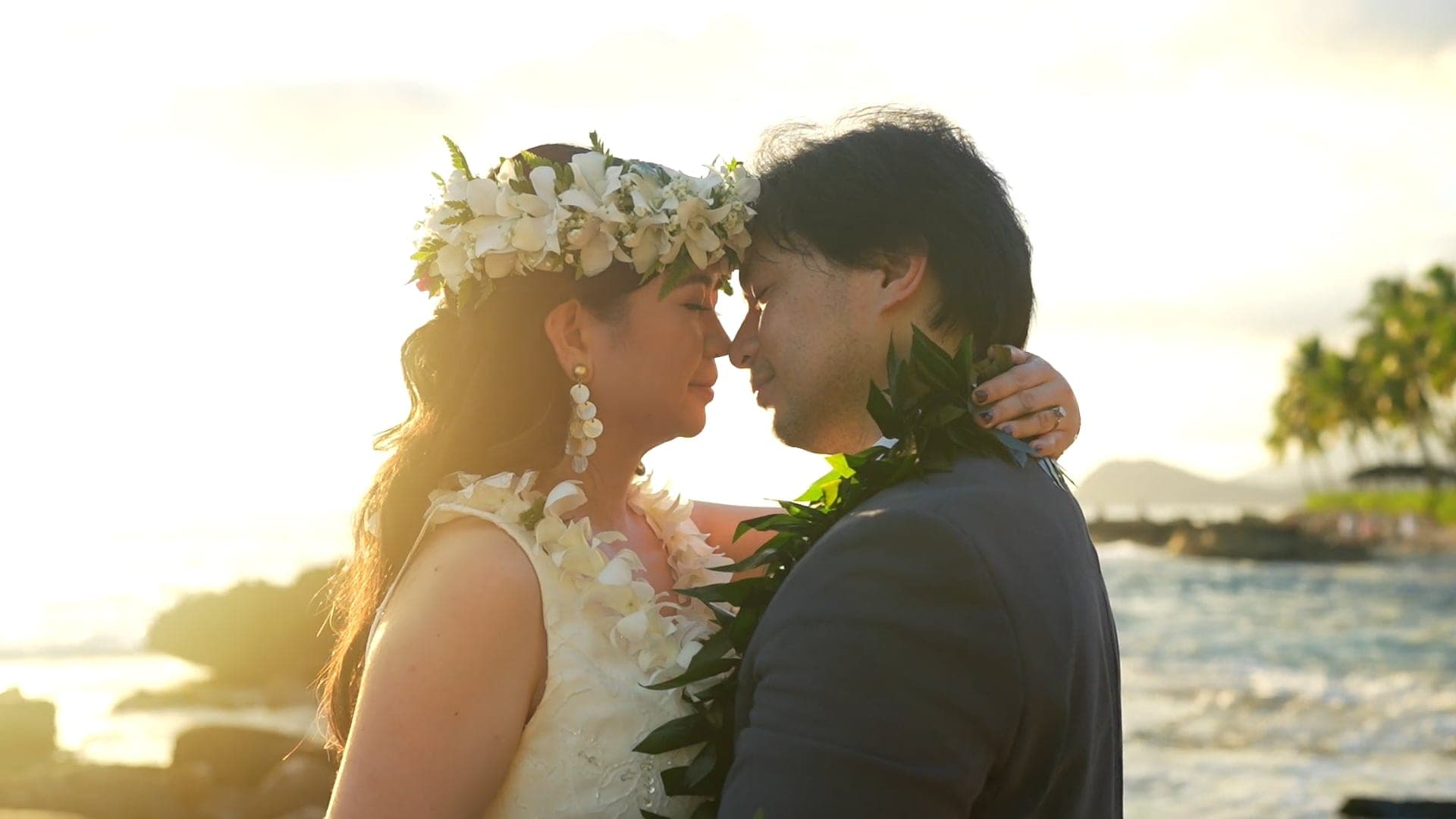 Leslie and Andy rest their foreheads together by the ocean in golden sunset light.