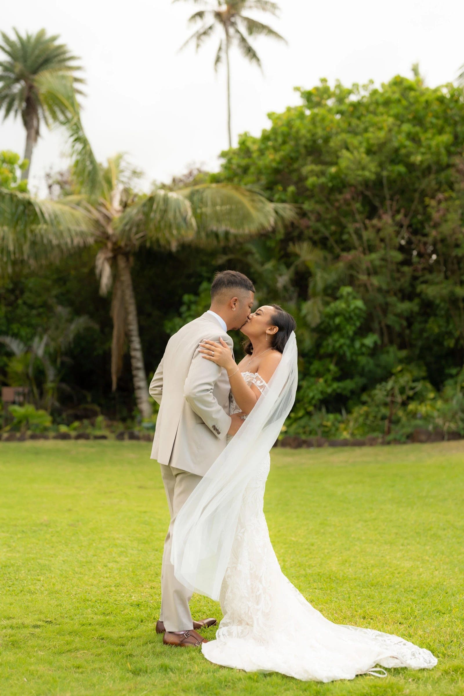 The groom dips the bride for a kiss on the lawn under the palms, her veil trailing.