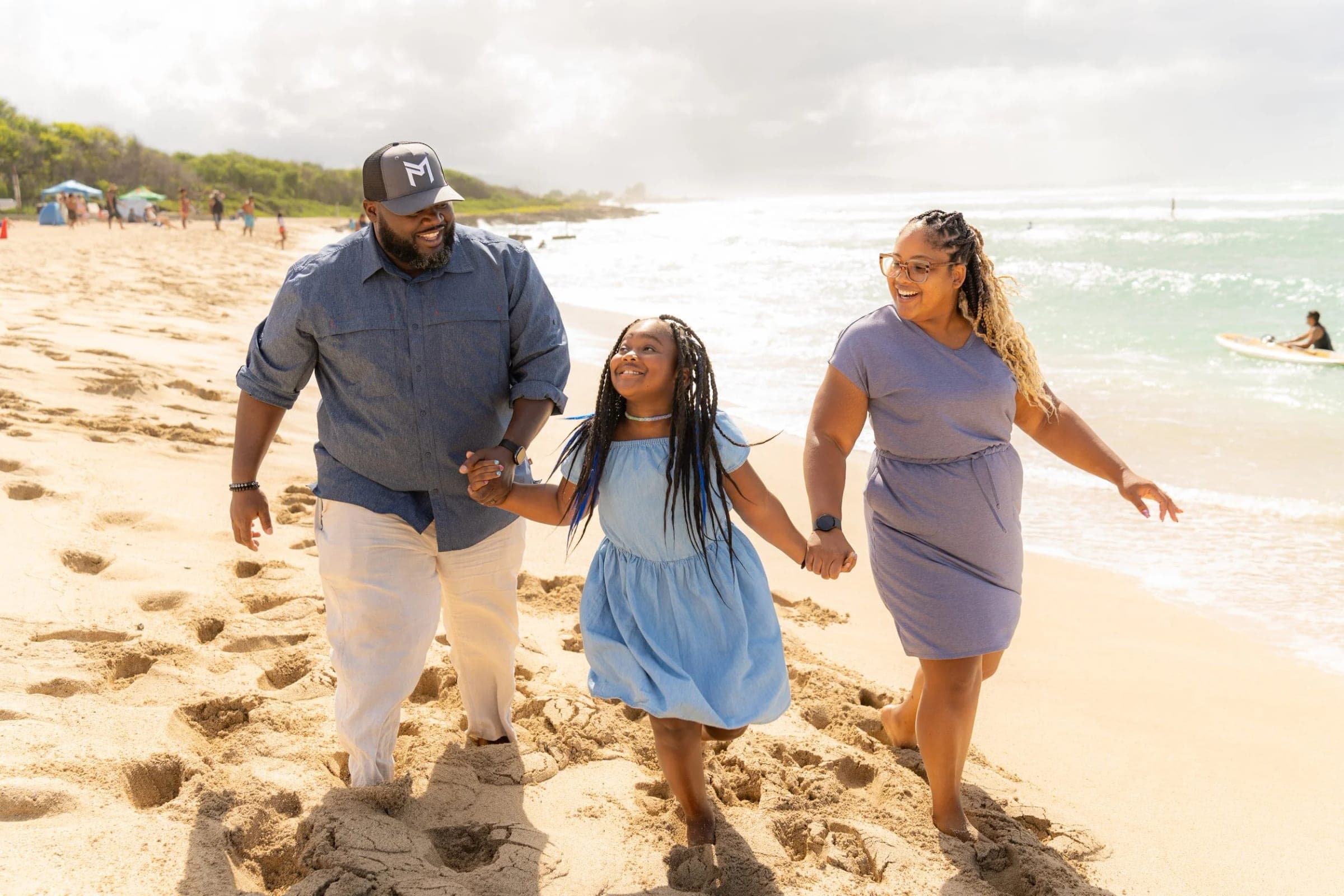 A family walk and laugh together along a beach, holding hands.
